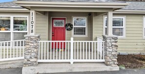 Une maison avec une porte rouge, des piliers en pierre et une clôture blanche en bois.