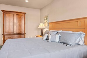 Une chambre à coucher avec un grand lit, une armoire en bois, une table de chevet avec une lampe et un tableau au mur.