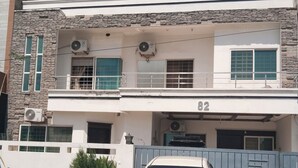 A two-story house with a white facade, stone accents, and a blue gate. - Capri Inn Guest House (Islamabad)