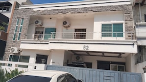 A two-story building with a stone facade, numbered 82, featuring balconies, air conditioning units, and a gated entrance. - Capri Inn Guest House (Islamabad)