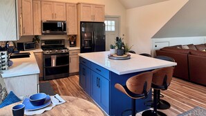 Cocina moderna con armarios de madera, una isla central, taburetes de bar y un comedor con mantel azul.