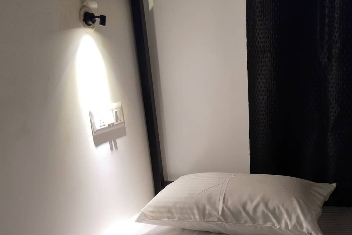 A bed with a white pillow and a wall-mounted light fixture.