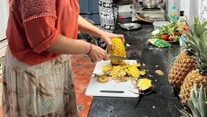 A kitchen with two people preparing food, a cutting board with pineapple slices, and a whole pineapple on the counter. - The Chill House (Kochi)