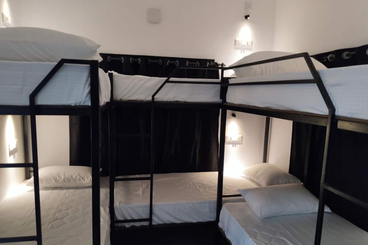 A bunk bed room with three beds, each with a pillow and a light on the side.