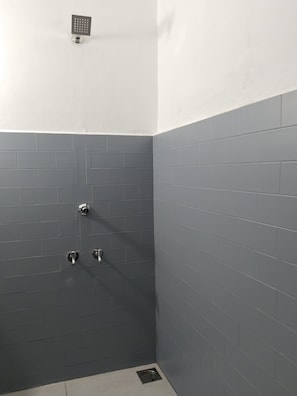A small, enclosed shower area with grey tiles and a single showerhead. - The Chill House (Kochi)