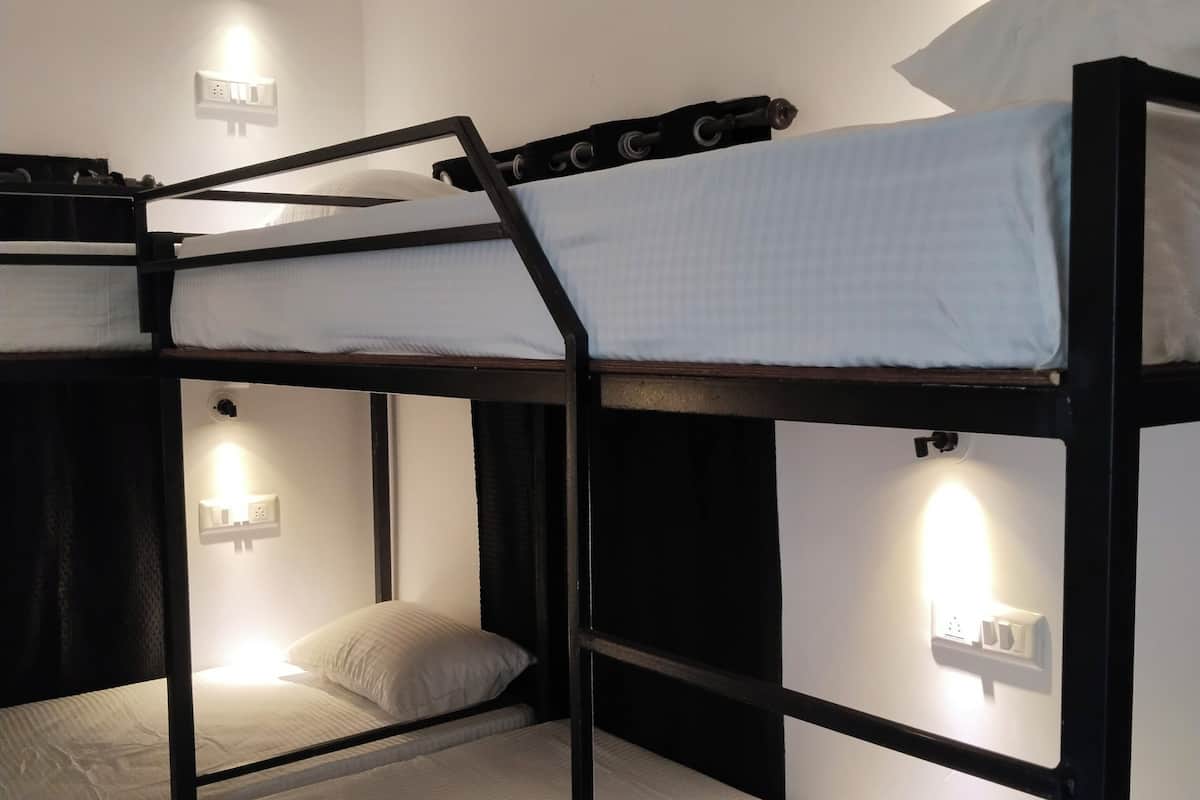 A bunk bed room with three beds, each with a pillow and a headboard. There are wall-mounted lights above each bed.