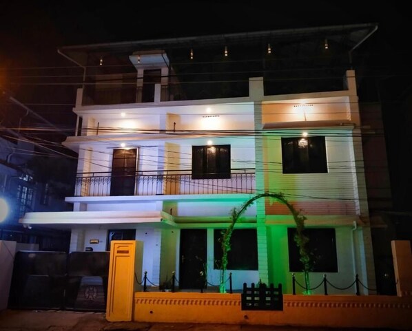 A multi-story building with balconies, a gated entrance, and a small garden area. - The Chill House (Kochi)