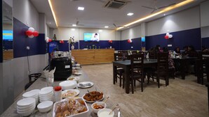 Un espace repas avec des tables et des chaises, un buffet garni de différents plats et un écran de télévision fixé au mur.