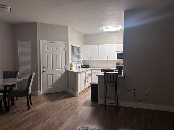A compact kitchen with white cabinets, a dining area with a table and chairs, and a small bar stool. - Contemporary Tempe Retreat: Modern Elegance with Poolside Luxury (mesa)