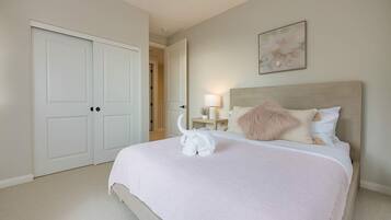 A bedroom with a large bed, a nightstand with a lamp, a painting on the wall, and a door leading to another room.