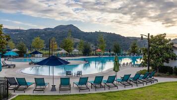 Une piscine entourée de verdure et de collines, avec des chaises longues et des parasols.
