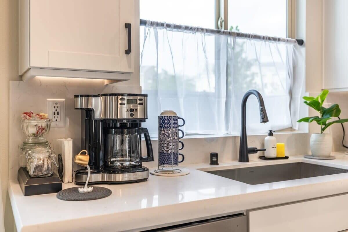 A modern kitchen with a coffee maker, a glass container, a patterned mug, and a sink.