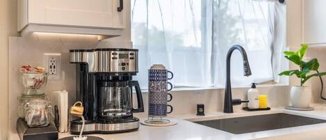A modern kitchen with a coffee maker, a glass container, a patterned mug, and a sink.