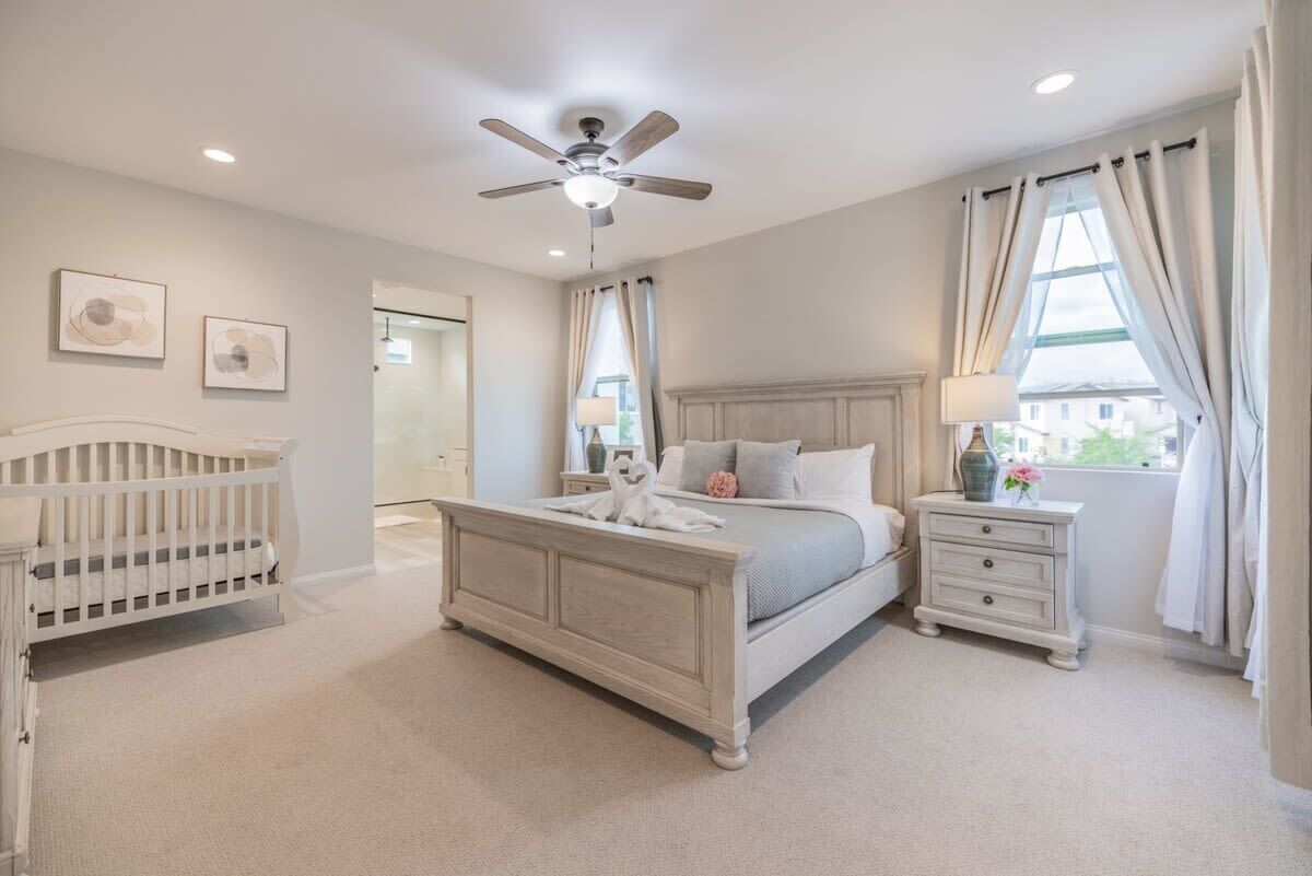 Quarto com cama, berço, mesa de cabeceira e ventilador de teto.
