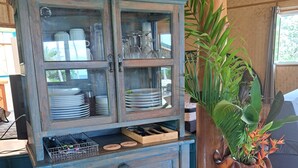 Un gabinete rústico de madera con puertas de cristal, estantes y cajones, situado en una habitación con suelo de madera y una planta grande.