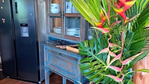 Una cocina con un armario de madera, un refrigerador y una planta en maceta con hojas rojas y verdes.