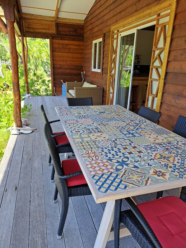 A covered patio with a long table, wicker chairs, and a view of the surrounding greenery.