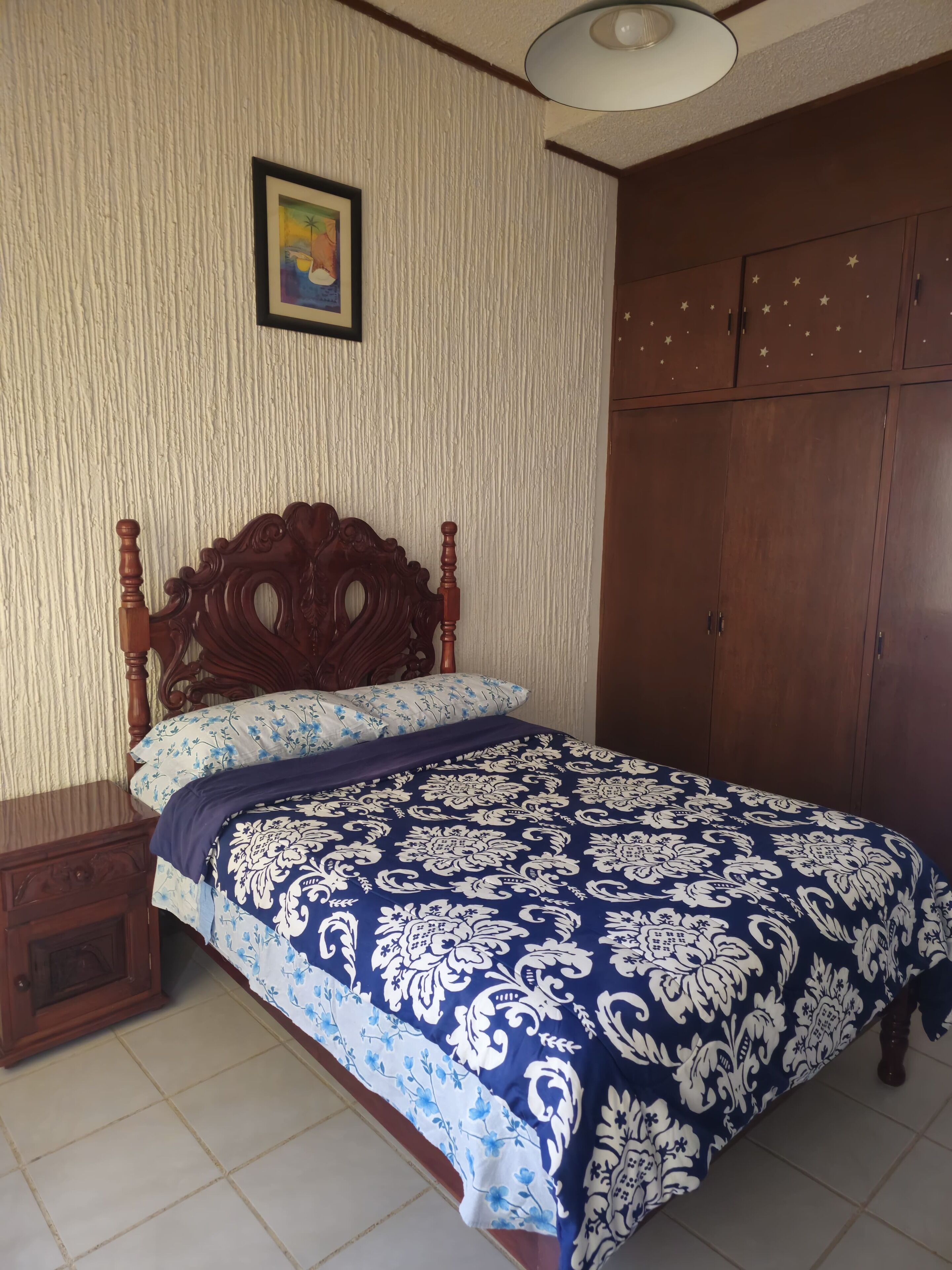 Une chambre à coucher avec un lit en bois, une table de chevet, une armoire et un tableau encadré au mur.