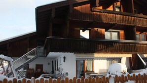 Een houten chalet met balkon, trap en een met sneeuw bedekte omheining.