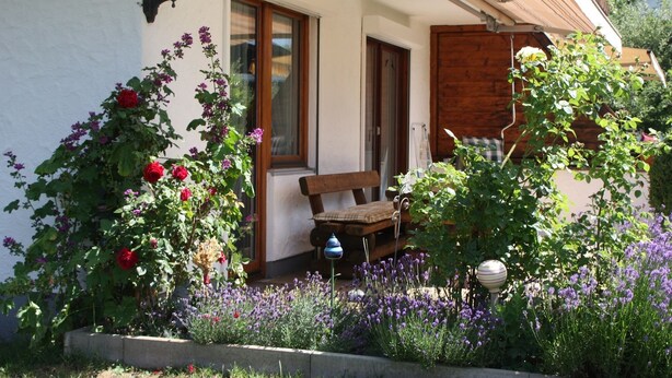 Een charmant huis met een houten bankje voor, omringd door kleurrijke bloemen en een tuin.