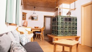 Een gezellige woonkamer met een houten plafond, een bank met decoratieve kussens, een eettafel en een groene speaker.