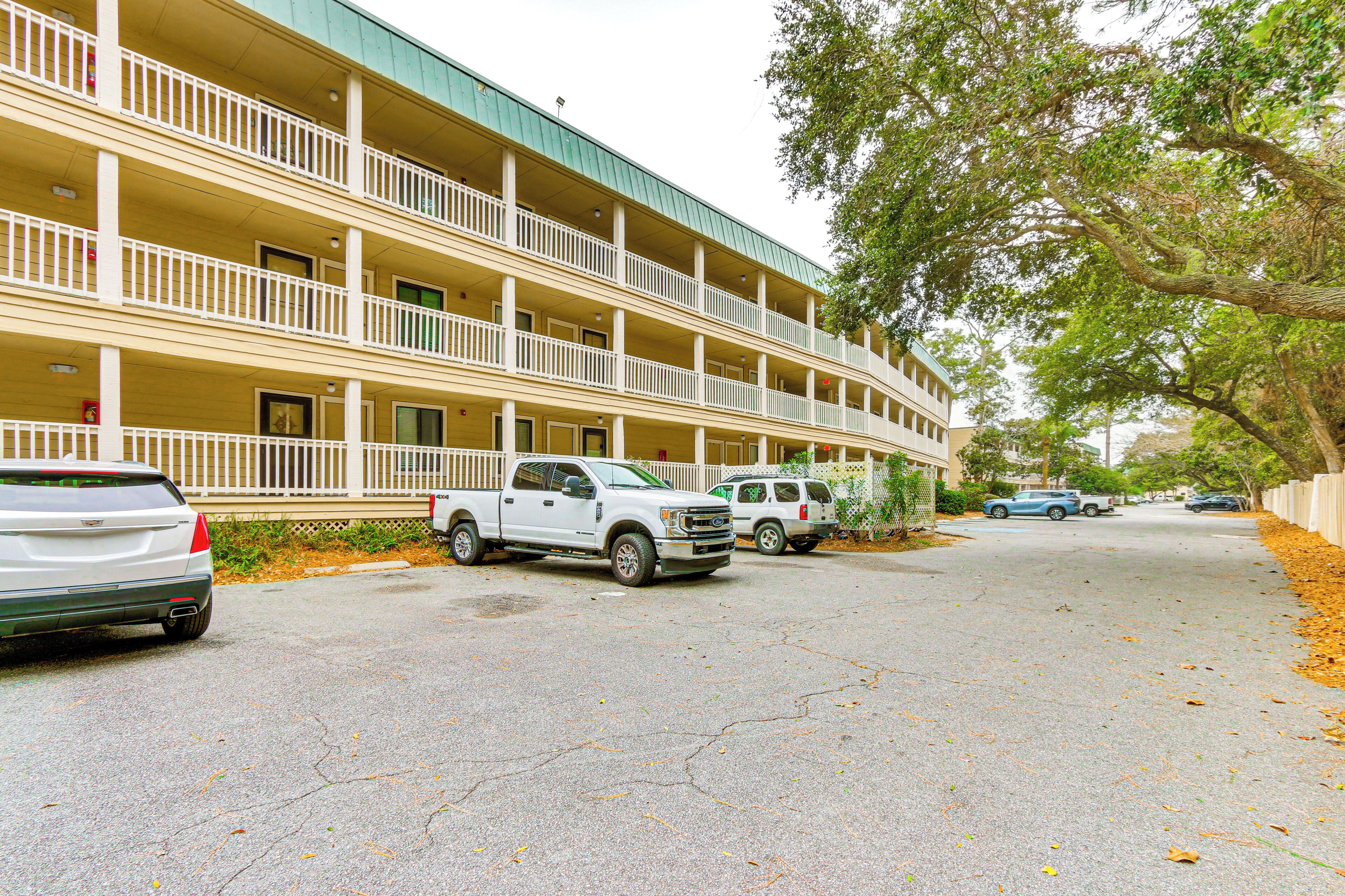 A multi-story hotel with balconies, parked vehicles, and a tree-lined street.