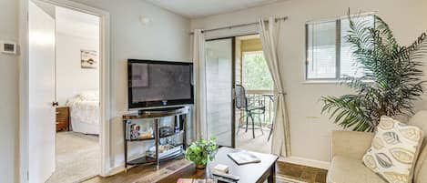 Un salón con televisor de pantalla plana, una mesa de centro, un sofá, una planta en maceta y un ventanal corredero que da a un balcón.