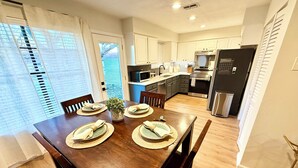 A modern kitchen with white cabinets, stainless steel appliances, and a dining area with a wooden table set for four. - Charming 3-bedroom Georgetown house close to Square. Long term stays welcomed. (Georgetown)