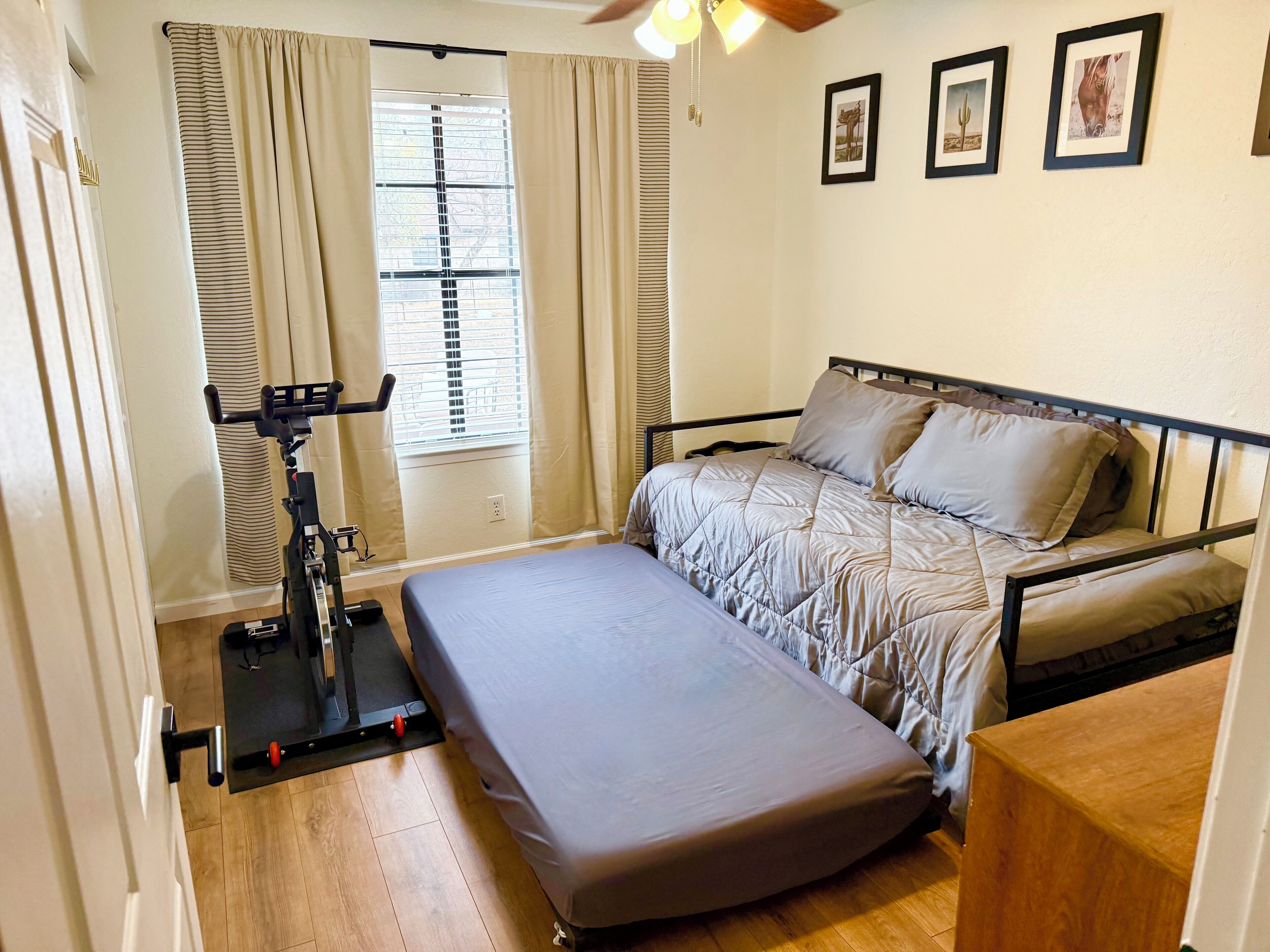 Ein Schlafzimmer mit Bett, Fitnessrad und einem Fenster mit Vorhängen.