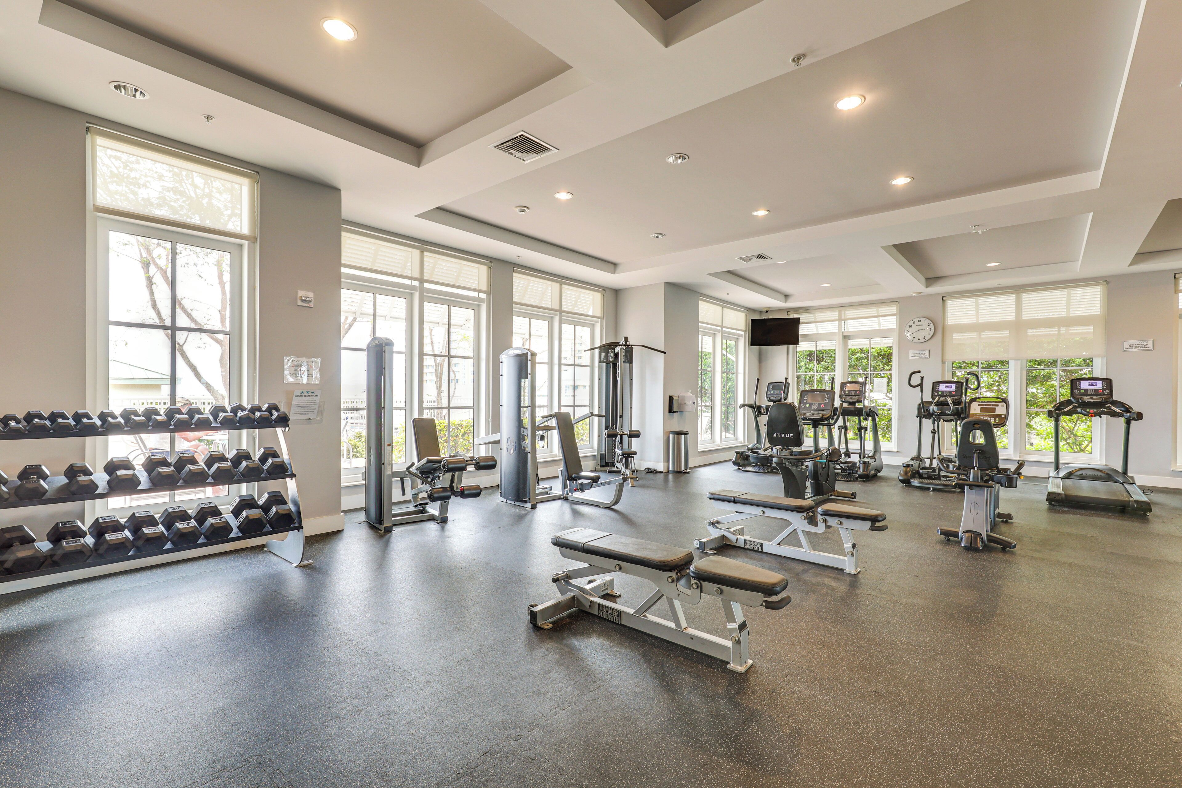 A spacious gym with various exercise equipment, large windows, and a clean, modern design.