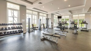 Une salle de sport spacieuse, dotée de divers appareils d’exercice, de grandes fenêtres et d’un aménagement propre et moderne.