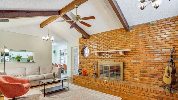 A living room with a brick fireplace, a ceiling fan, and a guitar leaning against the wall.