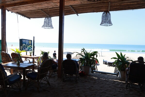 Un restaurant situé en bord de mer, avec des chaises et des tables en osier, offrant une vue sur l’océan.