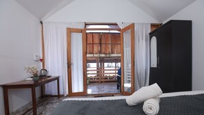 A bedroom with a bed, a desk, and a view of an outdoor wooden deck. - Silent waves (Canacona)