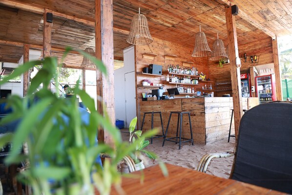 A rustic wooden interior with a bar area, wooden stools, and a refrigerator. - Silent waves (Canacona)