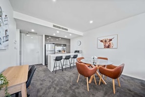 A modern kitchen with a central island, bar stools, and a dining table with chairs.