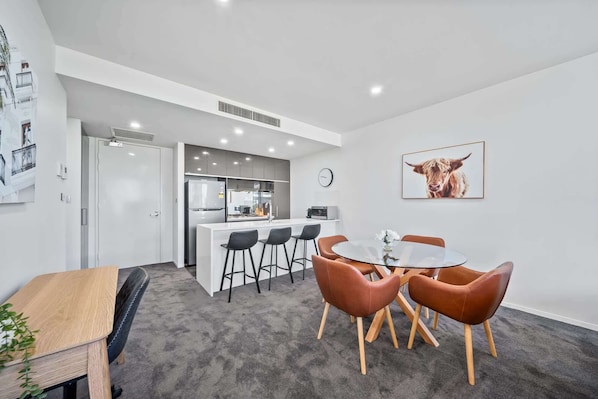 A modern kitchen with a central island, bar stools, and a dining table with chairs.