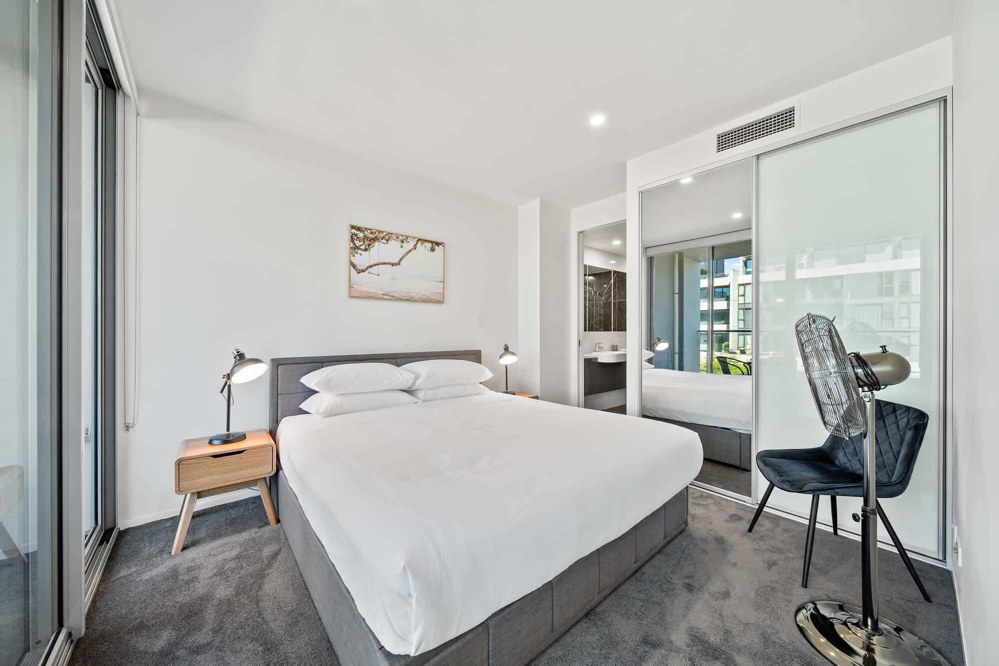 Ein modernes Hotelzimmer mit einem großen Bett, Nachttischen, einem Sessel und Blick auf die Stadt durch eine Glastür.