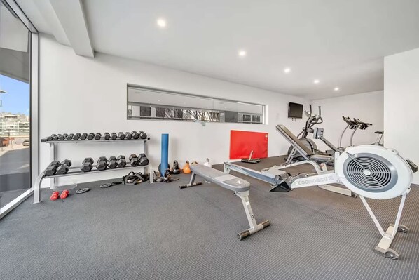 A modern gym with exercise equipment, a wall-mounted mirror, and a large window.