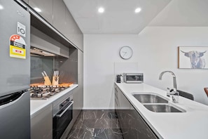 A modern kitchen with stainless steel appliances, a marble floor, and a clock on the wall.