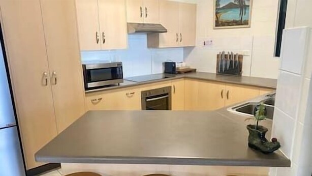Een keuken met een centraal eiland, houten krukken en een magnetron.