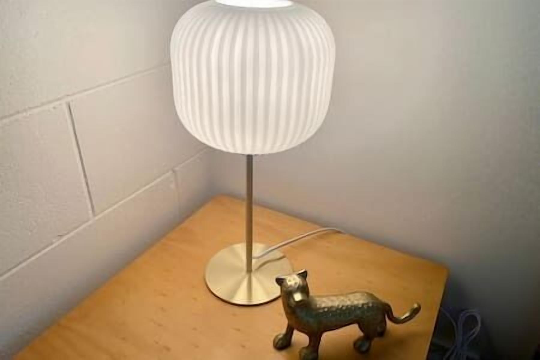 Una lámpara con pantalla estriada sobre una mesita de noche de madera.