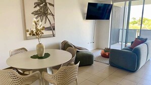Een moderne woonkamer met een ronde tafel, rieten stoelen, een bank en een flatscreen televisie aan de muur.