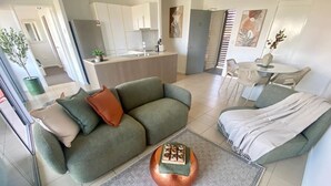 Een moderne woonkamer met een groene bank, een ronde koperen salontafel en een grijze vloerkleed.