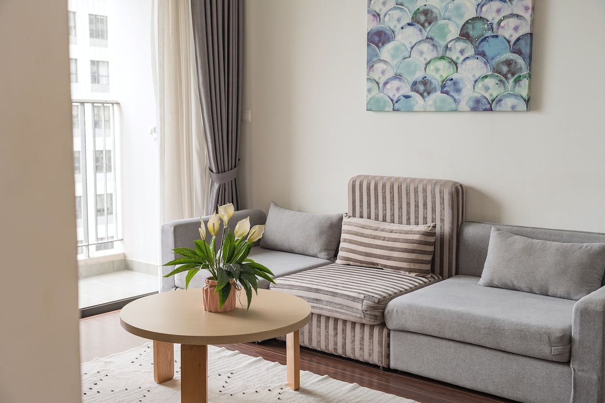 Een moderne woonkamer met een grijze bank, een ronde houten tafel en een plant in een pot.