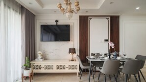 A modern dining area with a large TV mounted on the wall, a dining table set with chairs, and a decorative plant.