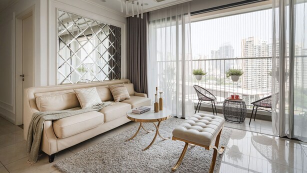 A modern living room with a beige sofa, a round coffee table, and a balcony with chairs and plants.