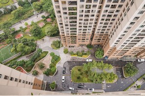 Un immeuble de grande hauteur doté de nombreux balcons, une cour intérieure agrémentée de verdure et un espace de stationnement.