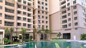 A modern multi-story building with a swimming pool surrounded by palm trees and greenery.