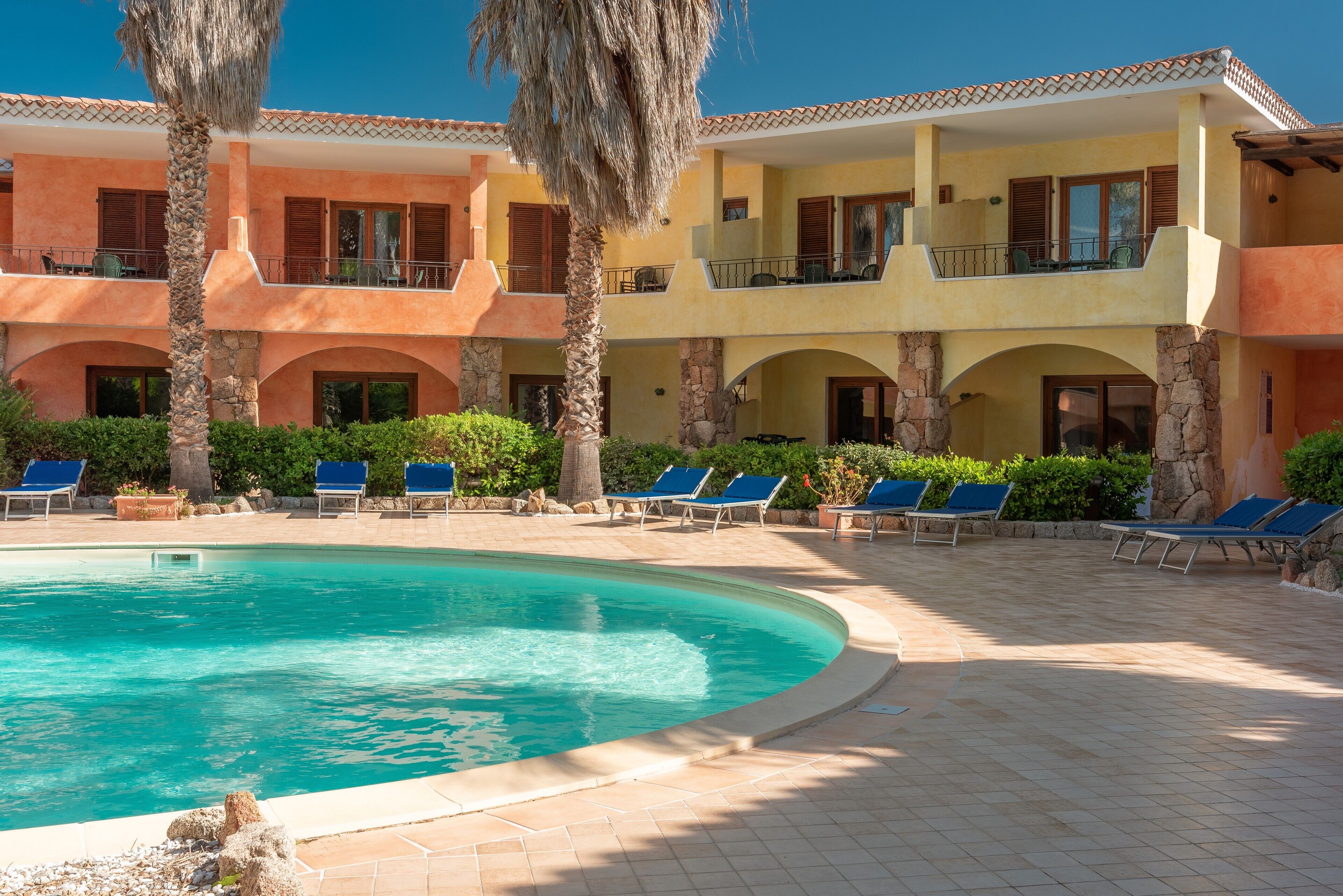 Zona de piscina con sillones reclinables y un edificio con balcones.